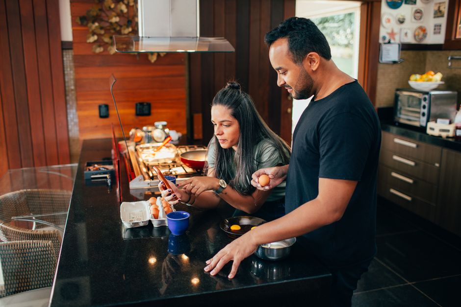 A couple sits at a bright, modern kitchen island with a laptop and coffee, happily planning a vacation, symbolizing using their home's value for life experiences.
